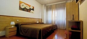 Un dormitorio con cabecera de madera, dos camas, una mesita de noche con lámpara, un armario de madera y un cuadro en la pared.