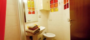 Ein Badezimmer mit Waschbecken, Spiegel und einem kleinen Fenster mit rötlicher Glasbeschichtung.