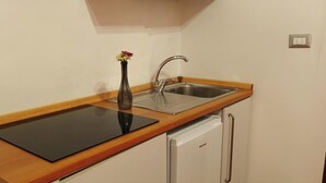 A compact kitchen with a sink, a vase with flowers, and a dishwasher.