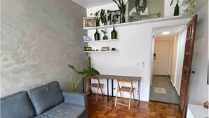 A living room with a grey sofa, wooden parquet flooring, a dining table with chairs, and a white wall with shelves holding decorative items. - Charming 1-bedroom loft in downtown Rio de Janeiro. (Rio de Janeiro)