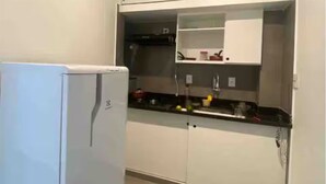 A compact kitchen with white cabinets, a refrigerator, and a countertop with various items. - Charming 1-bedroom loft in downtown Rio de Janeiro. (Rio de Janeiro)