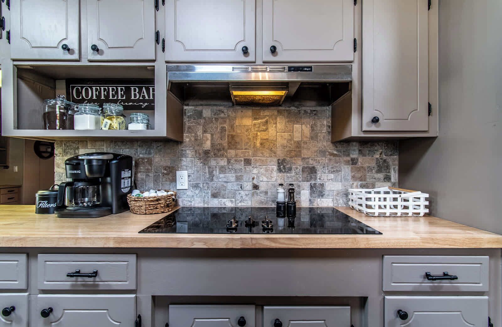 A kitchen with a stone backsplash, a coffee bar, and a Keurig coffee maker.