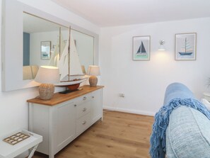 Ein Zimmer mit Holzboden, einem weißen Schminktisch, einem Spiegel, zwei Lampen und zwei gerahmten Bildern von Segelbooten an der Wand.