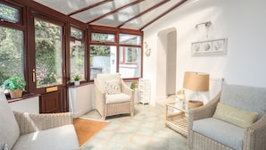 A sunlit room with wicker furniture, a glass ceiling, and a view of greenery outside. - Red Wharf Retreat (Pentraeth)