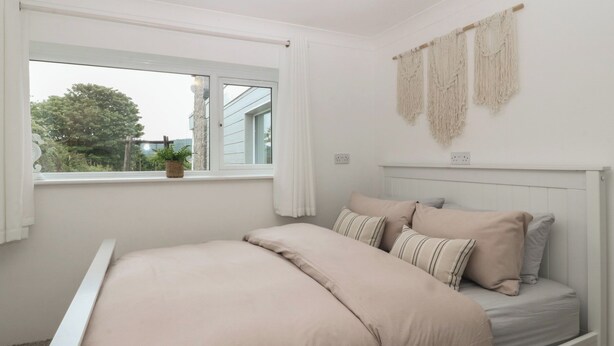 A bedroom with a bed, a window with curtains, and a wall-mounted macrame piece. - Red Wharf Retreat (Pentraeth)