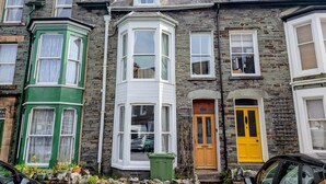 Une rangée de maisons mitoyennes aux styles architecturaux distincts, dont une maison d’angle peinte en vert, dotée d’une baie vitrée et d’une porte jaune.