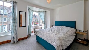 Une chambre à coucher avec un lit, une fenêtre avec des rideaux, une vue sur les bâtiments à l’extérieur et un luminaire suspendu.