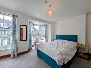 Ein Schlafzimmer mit einem Bett, einem Fenster mit Vorhängen, Blick auf Gebäude und einer Pendelleuchte.