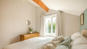 A bedroom with a bed, a wooden dresser, a window with curtains, and a mirror on the wall.