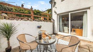A patio with wicker chairs and a table, a potted plant, and a sliding glass door leading to an interior space.