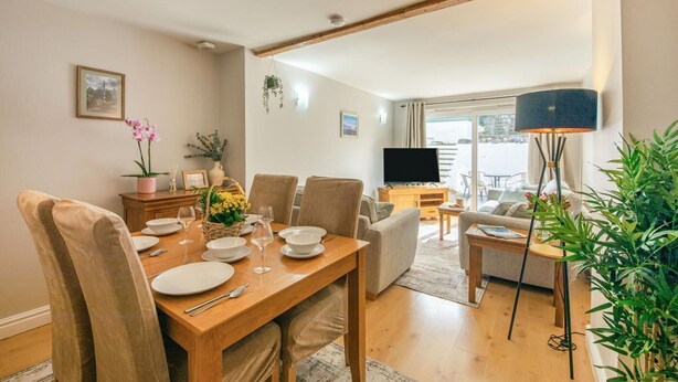 A dining area with a wooden table set for four, a television, and a sofa in the background.