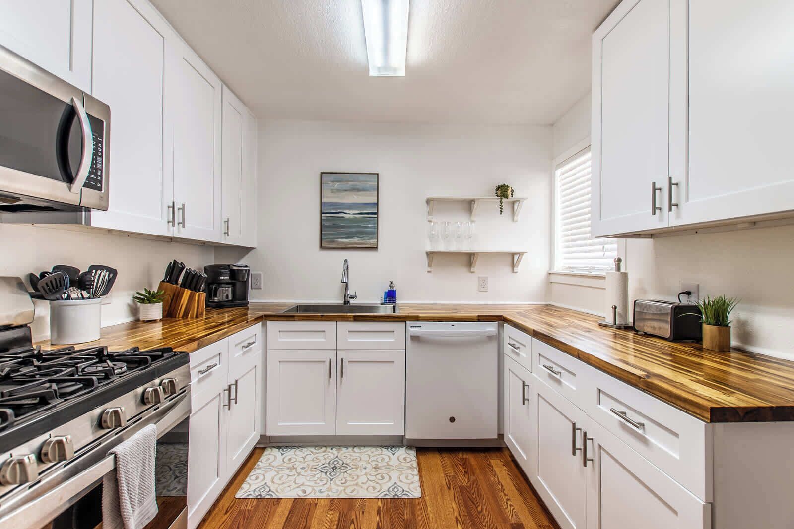 Une cuisine moderne avec des meubles blancs, un plan de travail en bois, un lave-vaisselle et une cuisinière.