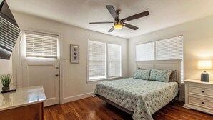 A bedroom with a bed, bedside tables, a ceiling fan, and a window with blinds. - Texas Tranquility Retreat (Corpus Christi)
