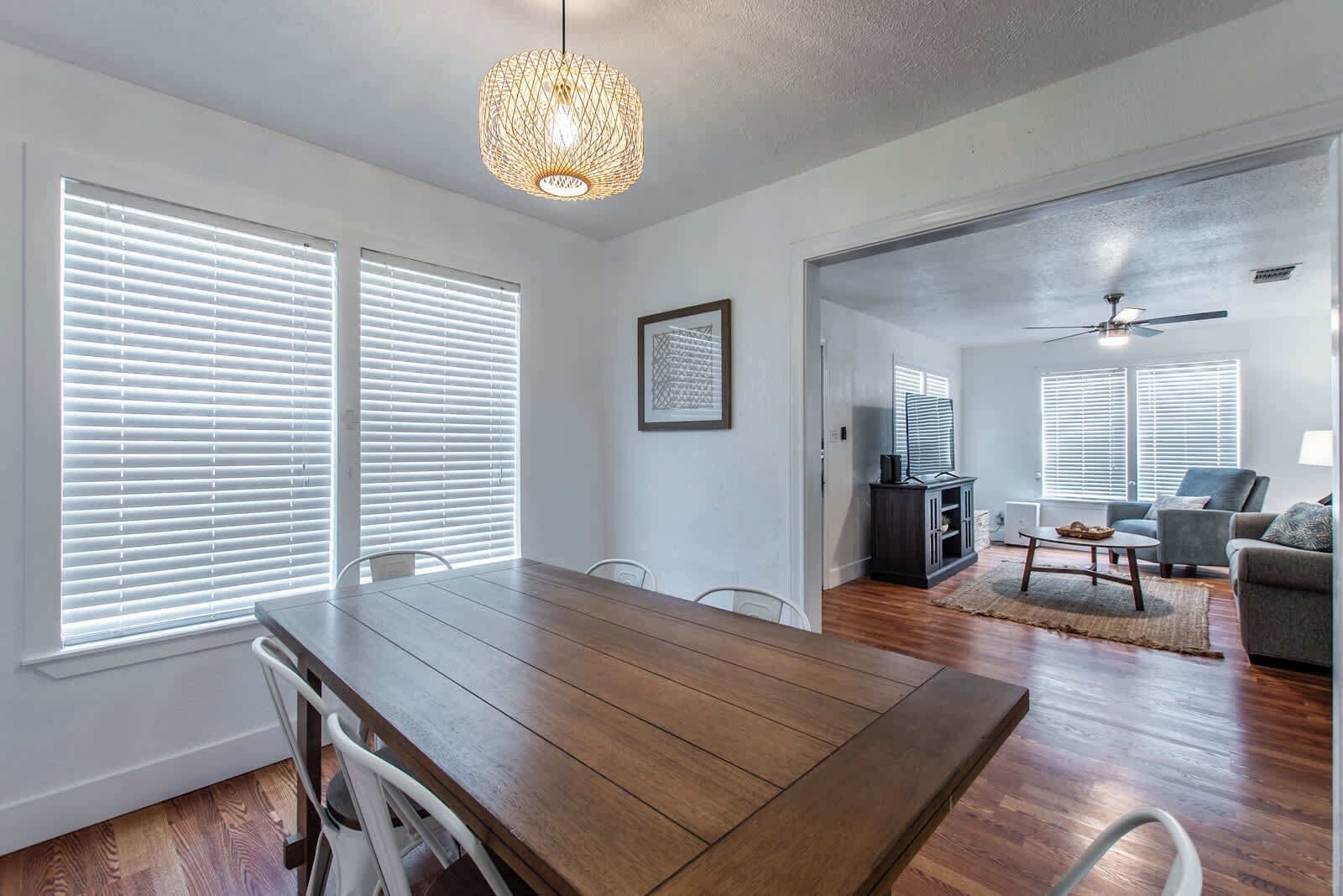 Un vaste espace de vie comprenant une table à manger en bois, des chaises blanches et un ventilateur de plafond.
