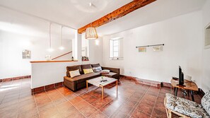 A living room with a brown sofa, a coffee table, a hanging light fixture, and a wooden ceiling beam.