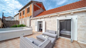 A rooftop patio with outdoor furniture, a stone wall, and a red-tiled roof.