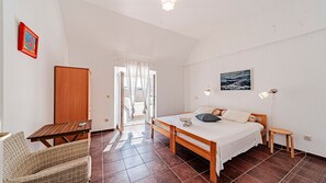 A bedroom with a bed, a desk, a chair, a wooden wardrobe, and a window with curtains.