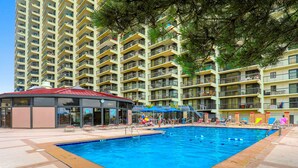 Una piscina con una struttura a tetto rosso, circondata da un edificio a più piani con balconi e un cielo sereno.