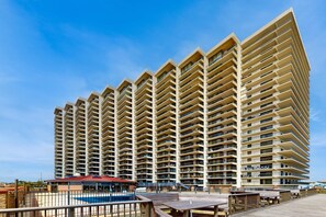 Ein Hochhotel mit mehreren Balkonen, einem Poolbereich und einer Promenade mit Sitzgelegenheiten.