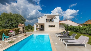 Ein modernes, zweigeschossiges Haus mit Swimmingpool, Sitzgelegenheiten im Freien und einem Garten.