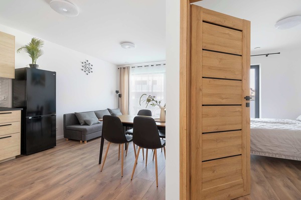 A perspective shot from the hallway looking into the bright living room and dining area. A wooden door frame structures the entrance to the main living space.