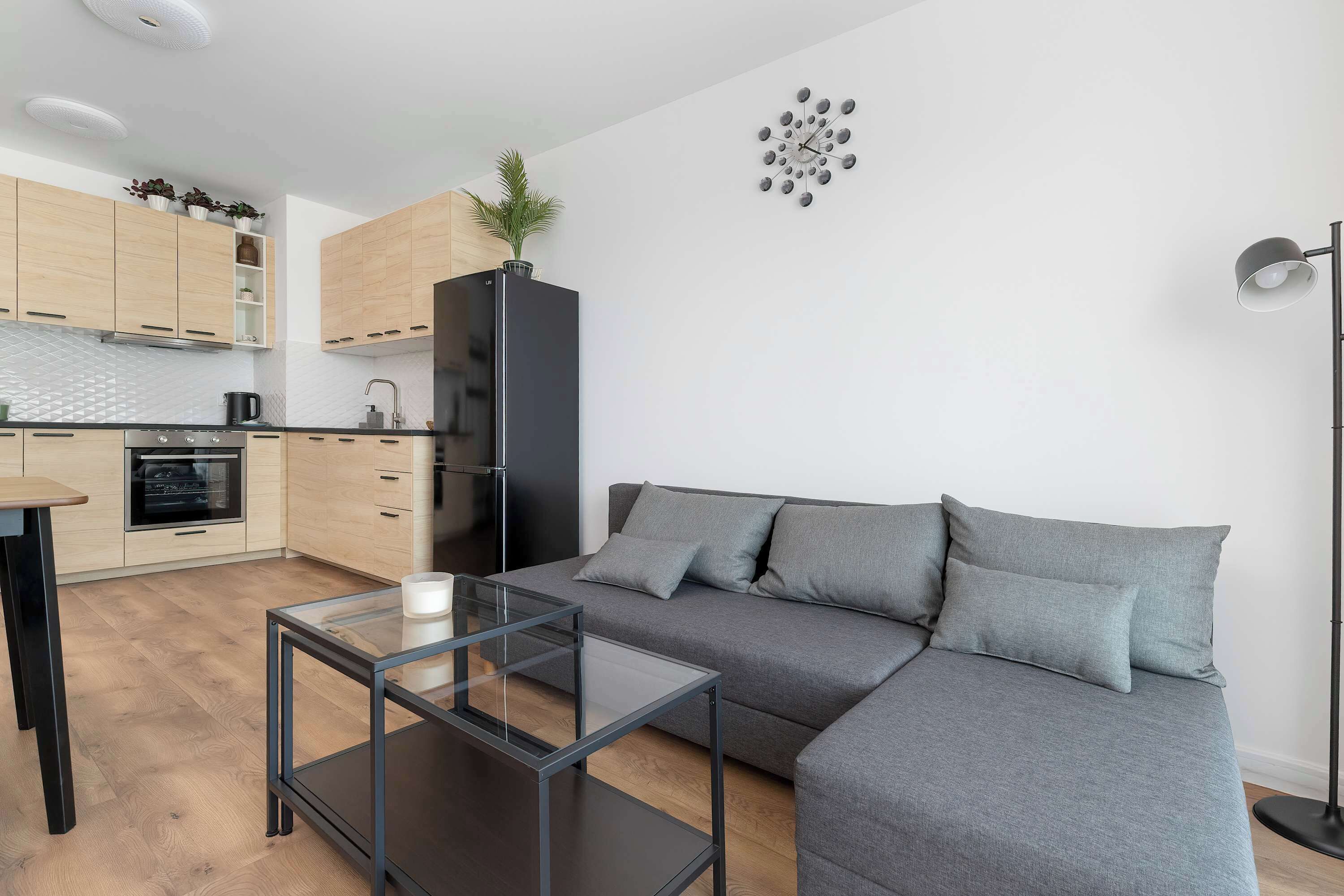 Un soggiorno moderno con cucina, divano, tavolino in vetro e lampada da terra.