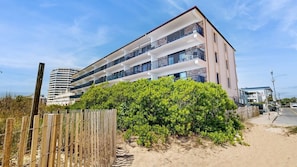 Ein mehrstöckiges Gebäude mit Balkonen, ein Sandstrand im Vordergrund und ein klarer Himmel.