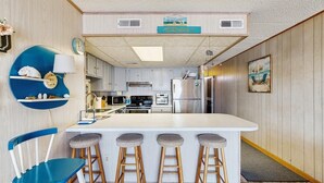 A kitchen with a central island, bar stools, wooden chairs, and a clock on the wall. - Bimini 306 (Ocean City)