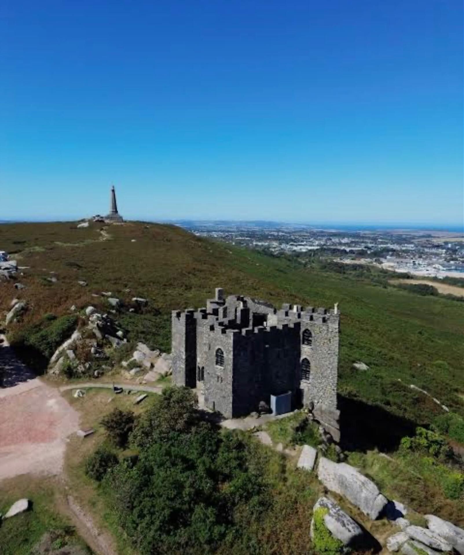 Ruinas de un castillo con una vista despejada del paisaje circundante, incluyendo un faro a lo lejos.