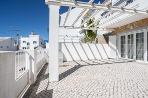 Ein weißes Gebäude mit überdachter Terrasse, Steinwand und blauem Himmel.
