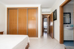 Ein Schlafzimmer mit Bett, Schrank, Badezimmer mit Waschbecken und einem Flur, der zu einem weiteren Raum führt.