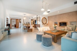 A spacious living area with a dining table, ottomans, and a sofa. - Villa 'Amarantos' with Mountain View, Wi-Fi and Air Conditioning (Santa Eulària des Riu)
