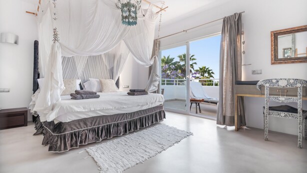 Ein Schlafzimmer mit Baldachinbett, einem Balkon mit Aussicht und einem Sessel.
