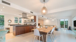 Eine moderne Küche mit Kochinsel, Essbereich mit Holztisch und weißen Stühlen sowie ein großes Fenster für natürliches Licht.