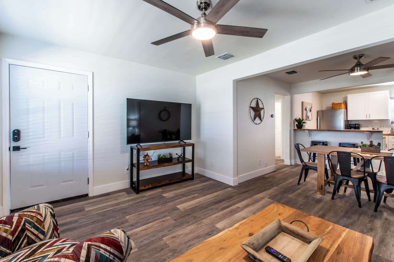 A modern living room with a flat-screen TV, wooden entertainment unit, and a dining area with a wooden table and chairs.