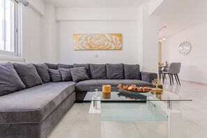 Ein modernes Wohnzimmer mit einem grauen Ecksofa, einem Glastisch und einer Wanduhr.