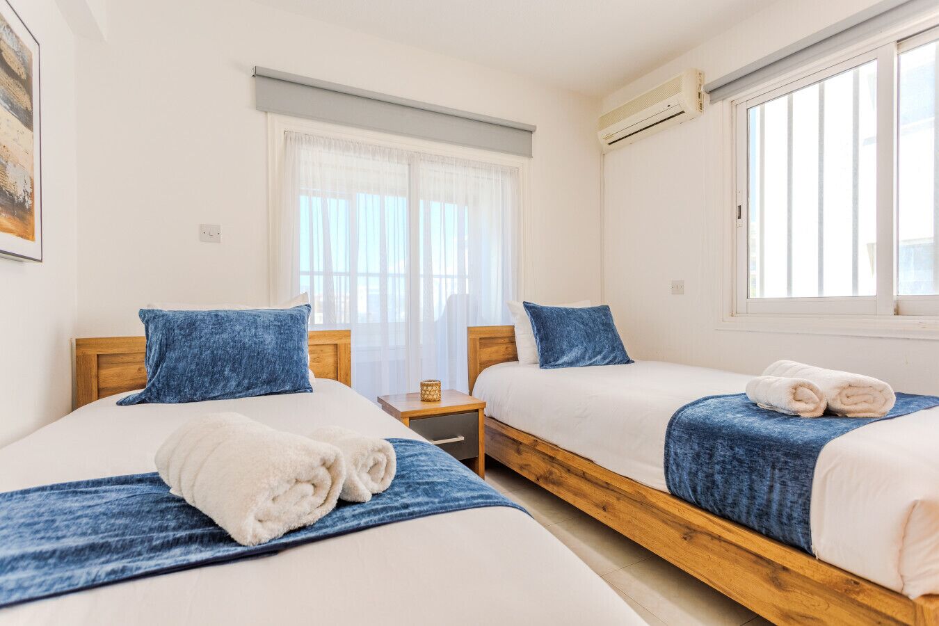 Habitació d'hotel amb dos llits, una finestra amb cortines, un aire condicionat i una taula petita amb una làmpada.