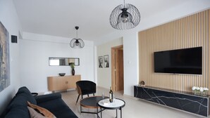 A modern living room with a black sofa, a round coffee table, a TV mounted on a wooden panel wall, and a pendant light. - TelMar Central Modern Retreat (Larnaka)