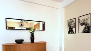 A modern interior with a wooden console, a vase with flowers, a mirror, and two wall art pieces. - TelMar Central Modern Retreat (Larnaka)