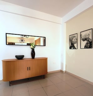 A modern interior with a wooden console, a vase with flowers, a mirror, and two wall art pieces. - TelMar Central Modern Retreat (Larnaka)