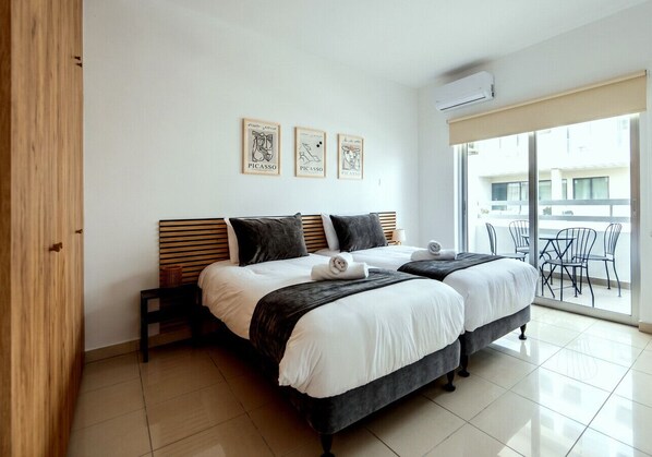 A double bed with a wooden headboard, two bedside tables, a large window with a view, and three framed artworks on the wall. - TelMar Central Modern Retreat (Larnaka)