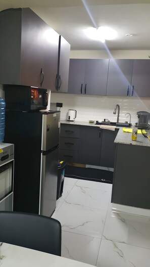 Eine moderne Küche mit grauen Schränken, einem schwarzen Kühlschrank, einer Mikrowelle und einer Kaffeemaschine.