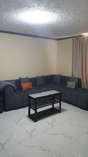 Ein Wohnzimmer mit Ecksofa, einem kleinen Couchtisch und einem Fliesenboden.