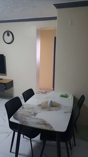 Ein Essbereich mit einem Marmortisch, schwarzen Stühlen, einem Fernseher an der Wand und einer Tür zu einem anderen Raum.