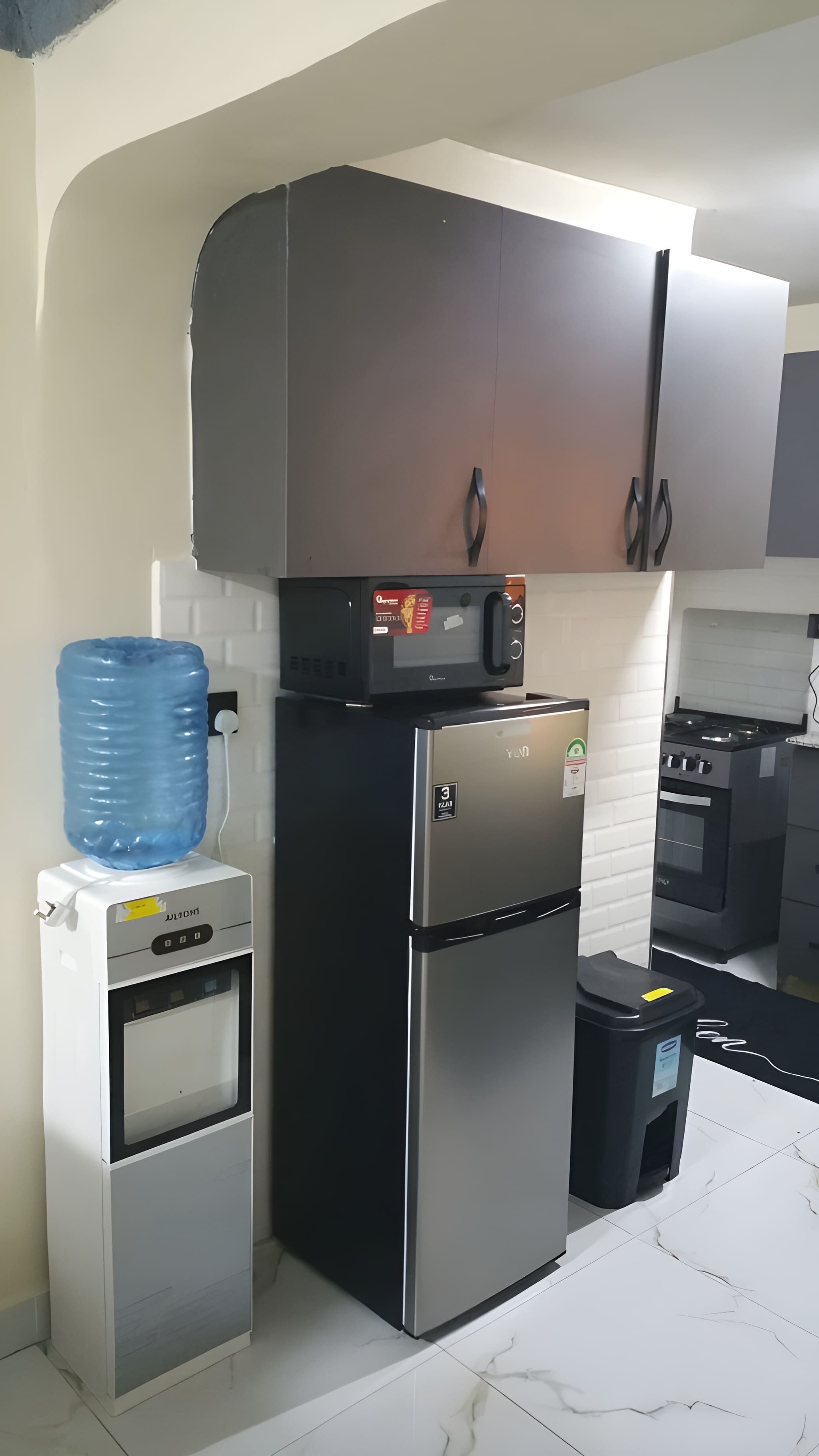 Une cuisine compacte équipée d’un réfrigérateur, d’un four, d’un four à micro-ondes et d’un distributeur d’eau.