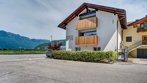 A modern building with a white facade, wooden balcony railings, and a parking lot. - Accessible Apartment '3' with Garden, Wi-Fi and Air Conditioning (Auer)
