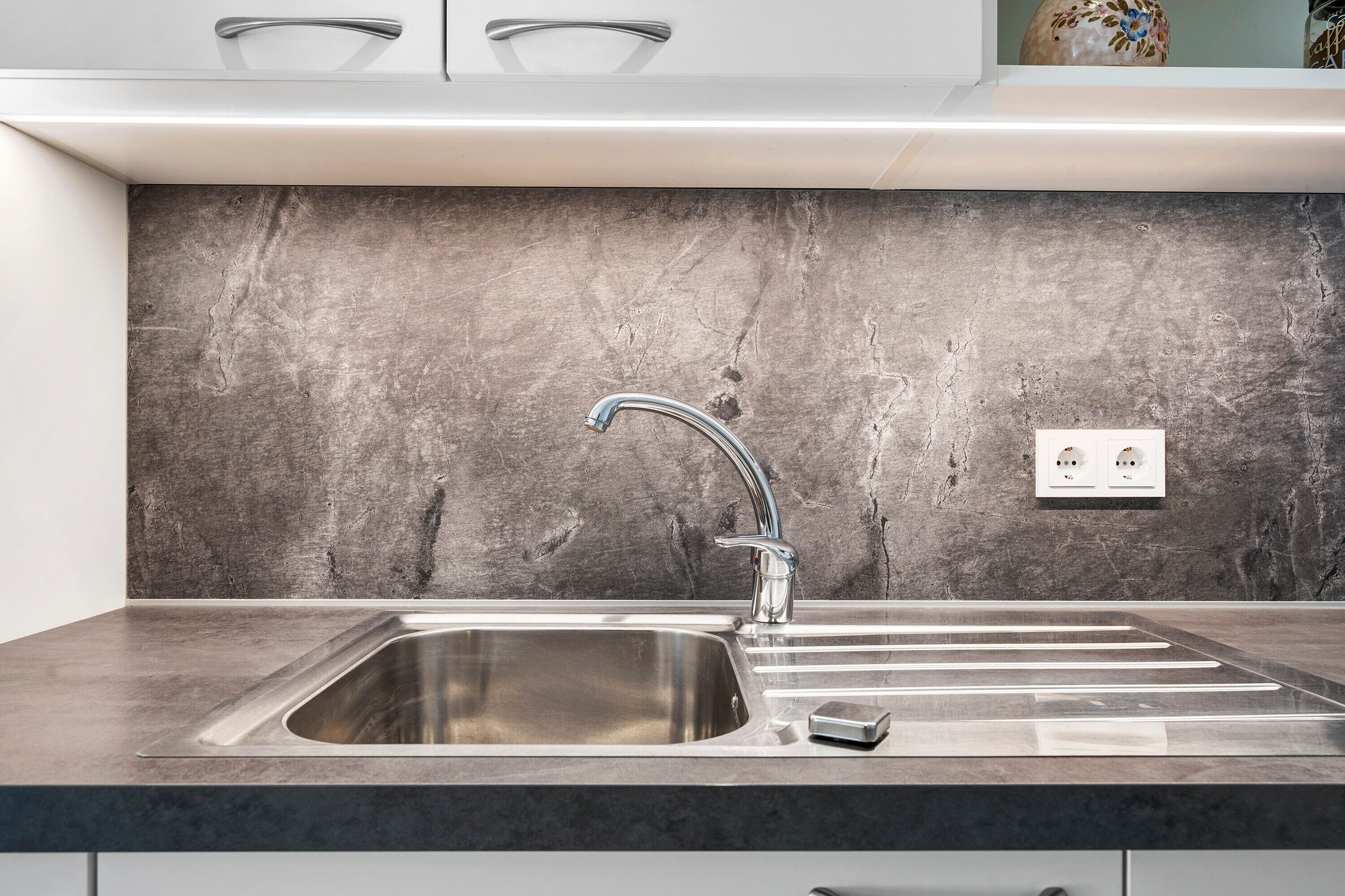 Een moderne keuken met een roestvrijstalen spoelbak, een marmeren achterwand en een strakke kraan.