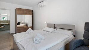 A modern hotel room with a large bed, a grey armchair, a mirror, and a built-in wardrobe. - Accessible Apartment '3' with Garden, Wi-Fi and Air Conditioning (Auer)