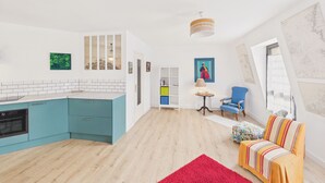 Eine moderne Küche mit türkisfarbenen Schränken, einem roten Teppich, einem blauen Sessel und einem farbenfrohen Sofa.