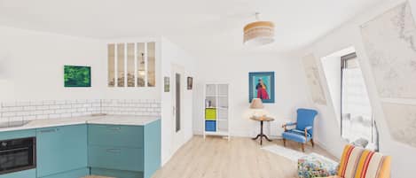 Una cocina moderna con armarios verde azulado, una alfombra roja, un sillón azul y un sofá colorido.